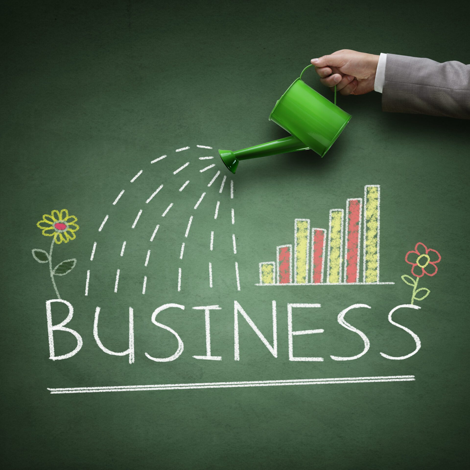 A green watering can being poured over the word ‘Business’ with flowers and a graph in chalk.